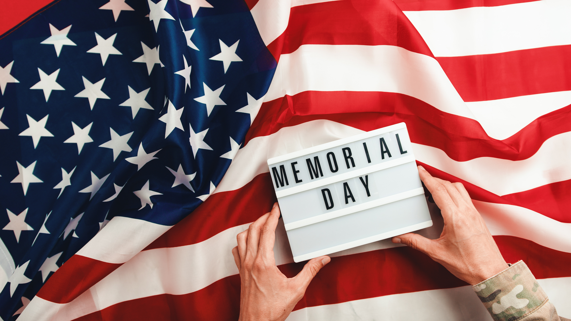Memorial day background with united states flag on the table Hands holding a sign that says "memorial day" against an american flag backdrop.