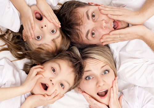 A family laying on a bed with their mouths open.