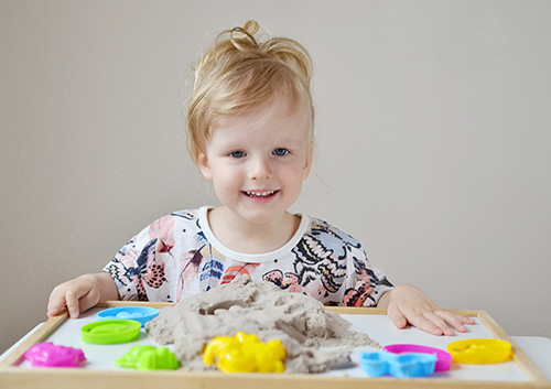 A little girl is playing with a sand tray.