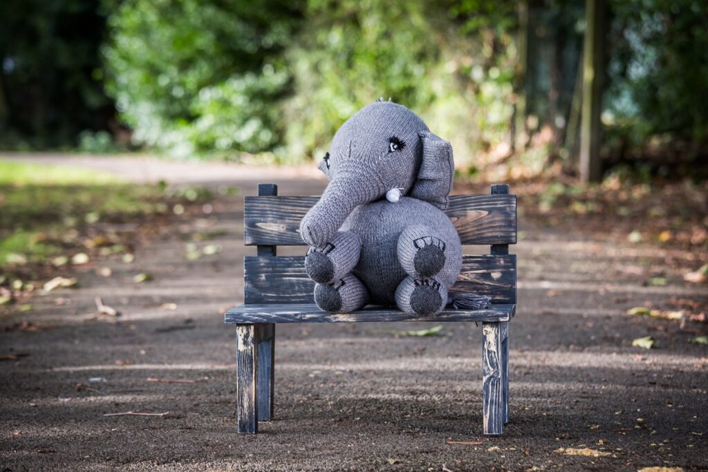 A stuffed elephant sitting on a wooden bench.