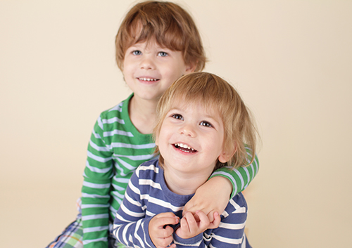 Two young children sitting on a beige background.