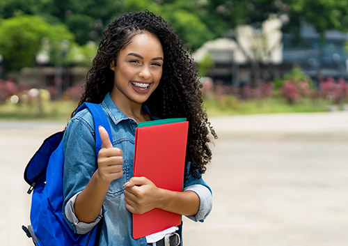 A young woman giving a thumbs up with a backpack.