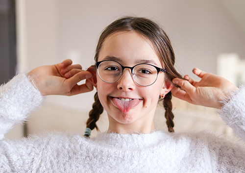 A girl with glasses is sticking her tongue out of her ear.