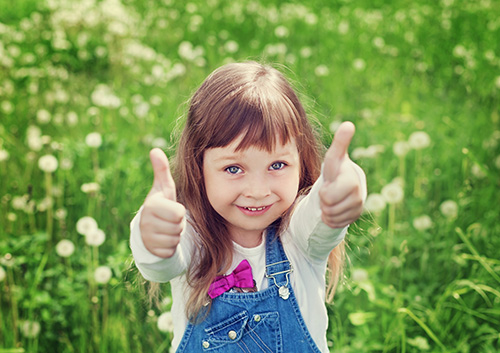 childrens_dental_health_month A little girl giving a thumbs up in a field.