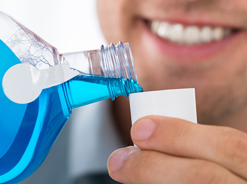 considerations_mouthwash_dreamstime_xl_72448419 A man is holding a bottle of blue liquid.