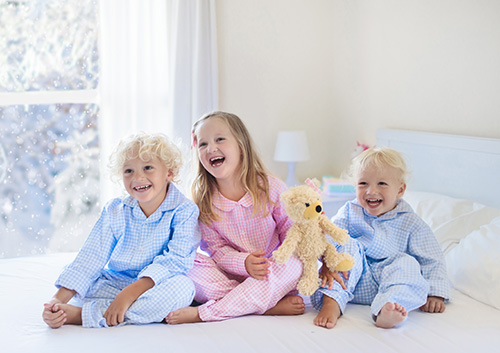 Three children in pajamas sitting on a bed with a teddy bear.