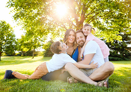 A family sits on the grass under a tree.