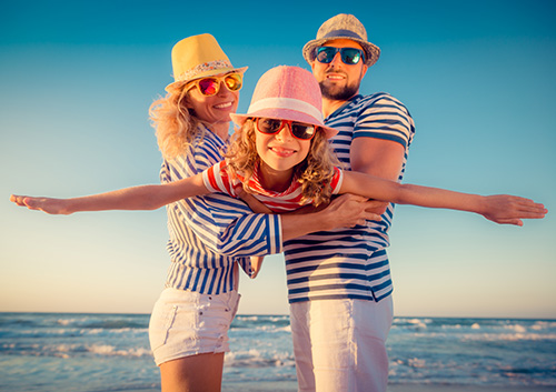 dental_emergency_traveling A family wearing striped hats and sunglasses on the beach.