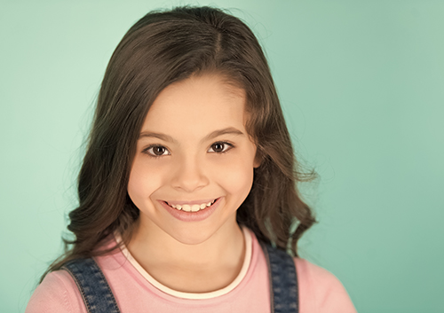 A young girl in overalls is smiling for the camera.
