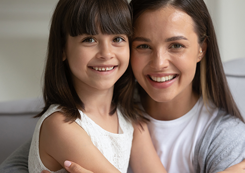 A woman and her daughter are smiling while sitting on a couch.