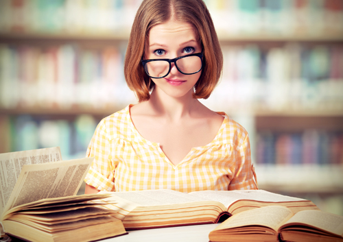A girl with glasses sitting at a table with books in front of her.