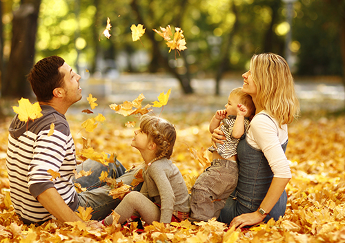 A family is playing in the leaves in a park.