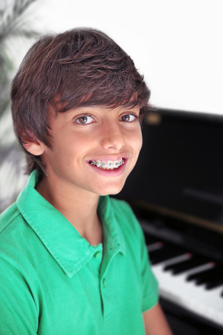 A young boy smiling in front of a piano.