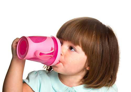 A little girl drinking from a pink cup.