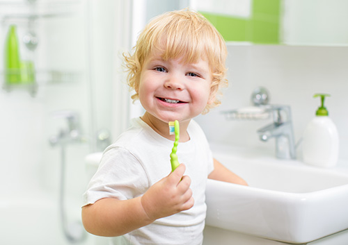 toothbrush_toothpaste_child A young boy holding a toothbrush in front of a sink.
