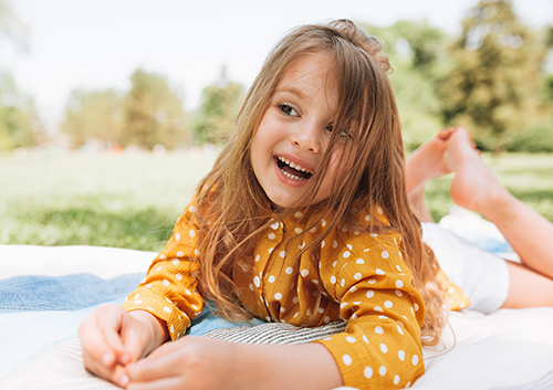 Smiling cute little girl lying on the blanket at green grass, ta A little girl laying on a blanket in a park.